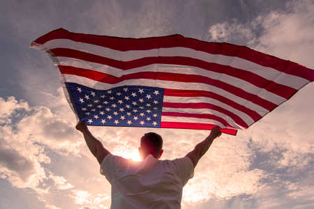 Man holding waving American USA flag in hands during warm sunny evening in USA, concept picture