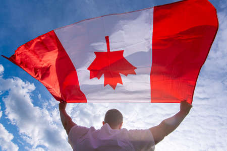 Man holding The National Flag of Canada against blue skyの写真素材