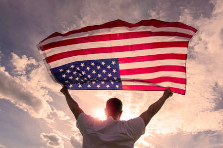 Man holding waving American USA flag in hands during warm sunny evening in USA, concept pictureの写真素材