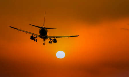 Silhouette of airplane during landing in front of amazing evening sky with sun, space for textの写真素材