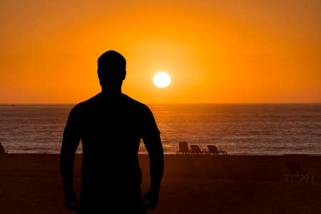 Silhouette of man, back side, in front of sea or ocean during sunset over water, concept picture
