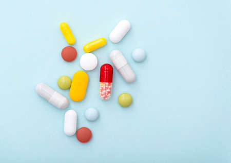 Medical composition. Some color pills on blue background, top view. Yellow, blue, green, red, white capsules, drugs.の写真素材