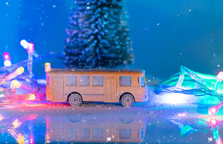 Miniature yellow bus and fir tree during snowfall, imitation of night time with garland. Christmas decoration, Christmas postcard with space for textの写真素材