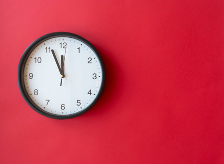 Round wall clock on red surface showing 12 o'clock, layout, top view, place for textの写真素材