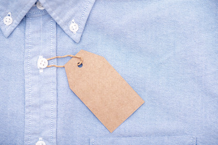 Blank paper label or tag on top of blue shirt, space for textの写真素材