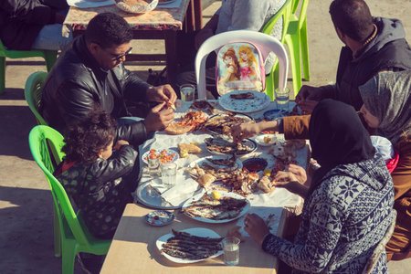 ESSAOUIRA - CIRCA JAN 2018: Moroccan family eating traditional seafood grilled sardine at a street cafe in Essaouira, January 2018 in Moroccoのeditorial素材