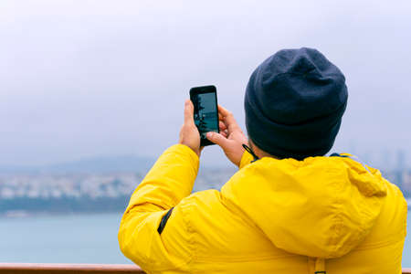 A man tourist taking photo by phone at the view point before Bosphorus in istanbul during winter dayの写真素材