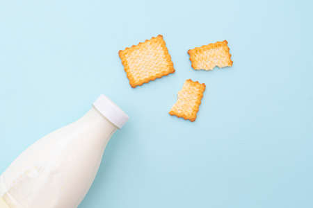 Broken dry cookies and bottle of milk on blue background, top view, lay out. Concept picture about food and breakfastの写真素材