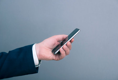 A man businessman dressed in suit holding smartphone in front of gray background. Business concept...