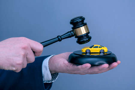 A man holding yellow car on wooden judge gavel, concept picture about car credit debt or divorce.