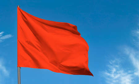 Bright red flag waving against blue sky, blank red bannerの写真素材