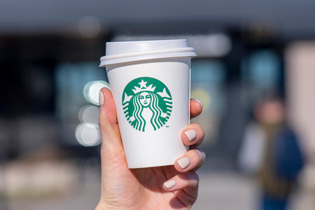 BERLIN - APR 17: A woman holding paper cup with Starbucks logotype in a street of Berlin, April 17.2021 in Germanyのeditorial素材