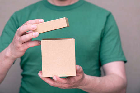 A man dressed in green t-shirt holding small paper cardboard box with open cap
