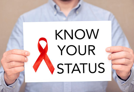 A man holding white sheet with a red ribbon on surface and text - know your status. Concept picture...