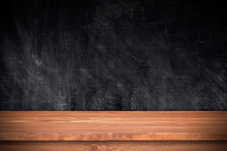 Wooden table with black wall as template. Empty brown tabletop and chalkboard, space for text, objectsの写真素材