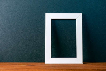Minimal interior composition with black wall and white blank photo frame on the wooden table, decor mockup, space for textの写真素材