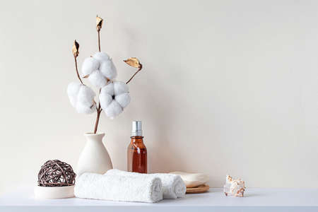 Bathroom interior in beige pastel tone. White shelf in bathroom with towels, soap, perfume bottle, cotton plant. Mockup with space for text. Minimal composition.の写真素材