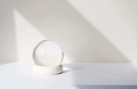 Minimal composition with glass ball on white desk, glass globe ball as decoration of interior. Abstract shadow lines on the wall, space for text, mockupの写真素材