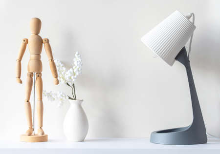 Interior of living room. Wooden mannequin, vase with decor plant, lamp on white wooden desk, mockup, minimal composition, space for textの写真素材