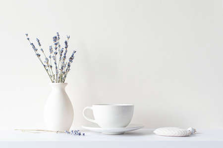 Still life with minimal composition, lavender dried bouquet, ceramic white cup and hot beverage tea or coffee, morning mood in beige toneの写真素材