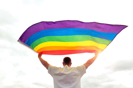 Proud man holding rainbow gay flag waving on the wind, concept picture about human rights and equalityの写真素材