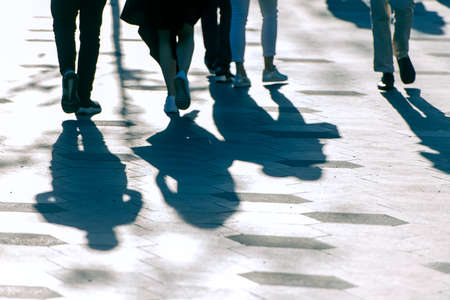 Shadows and silhouettes of people on a road during sunny evening.の写真素材