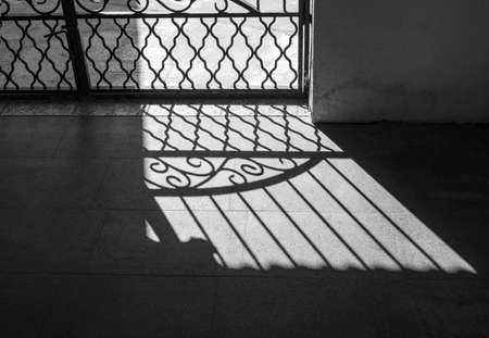 Lattice, grid infront of hard sunlight. Silhouette and shadow of iron fence. Texture background in black and white style.の写真素材