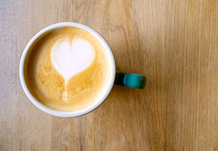 Coffee beverage with foam, latte or cappucchino. Ceramic cup with coffee and heart shape, top view. Cafe interiorの写真素材