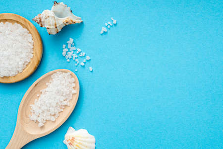 Sea salt, wooden spoon, shells on blue surface. Flat lay with crystals of salt, top view, space for textの写真素材