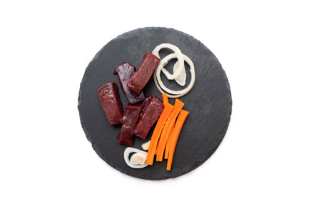 Pieces of raw liver meat with carrot and onion on the stone plate, top view, isolated on whiteの写真素材