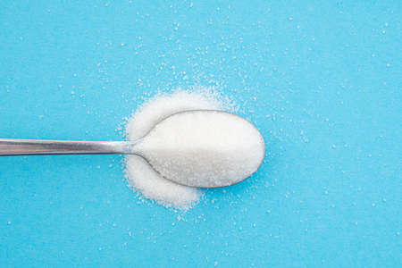 Close-up of a spoon with sugar heap, crystals of white sugar on blue background, top viewの写真素材