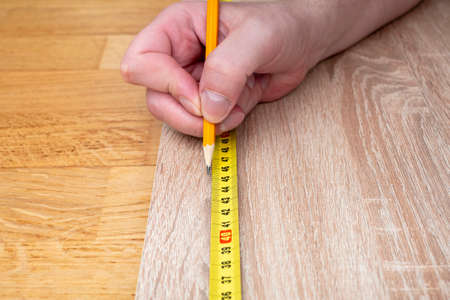 Close-up of hand of a carpenter measuring with a yellow ruler and drawing by pencilの写真素材
