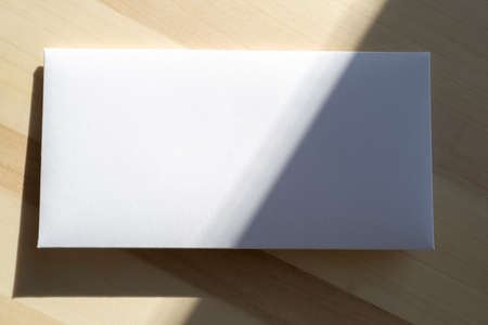 Blank white paper sheet, postcard, envelope as mockup and sunny light on surfaceの写真素材