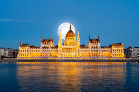 Amazing night view to Hungarian Parliament Building and Danube river with full moon over the city, art collageの写真素材