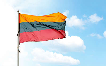 Large Lithuanian national flag on flagpole waving in wind against blue cloudy skyの写真素材
