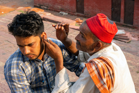 NEW DELHI - SEP 17: Indian street worker with a needle cleaning the ear to a person in a street in New Delhi, on September 17. 2022 in India.のeditorial素材