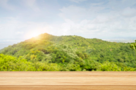 landscape with green hill, mountains, blue sky, sunrise and blank pine table, shelf for montage as display. Blurred nature background and board with perspective.の写真素材