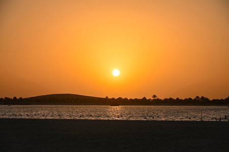 Sunset over desert and Abu Dhabi with sea and palm trees silhouettes, landscape as backgroundの写真素材