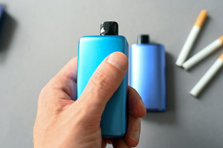 Person holding blue Electronic cigarette above table with analog cigarettes, conceptual picture about health and addictionの写真素材