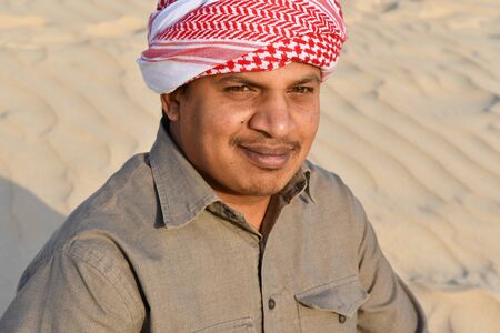 Portrait of a man with head scarf sitting on the sandの写真素材