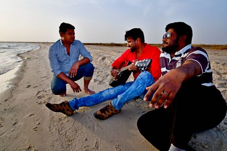 Guitar player playing with friends on a sandy beach at sunset timeのeditorial素材