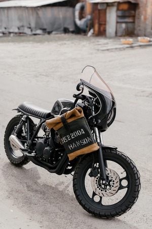Leather backpack near the motorcycle. Half black motorcycle in the garage. Motorcycle kaferacers.