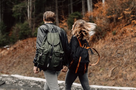 couple are traveling. Boy and girl with backpacks travel. The couple is on the road. Exclusive backpacks on the back. Flowing hair fluttering in the windの写真素材