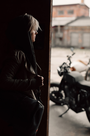 A young woman with a leather bag near the garage. A woman in a leather jacket. Motorcycle near the garage. Leather bag. Motorcycleの写真素材