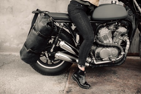 Woman sitting on his motorcycle. Motorcycle near the garage. Leather bag and jeans. Motorcycle black. The womans legs on a motorcycle. Bikeの写真素材