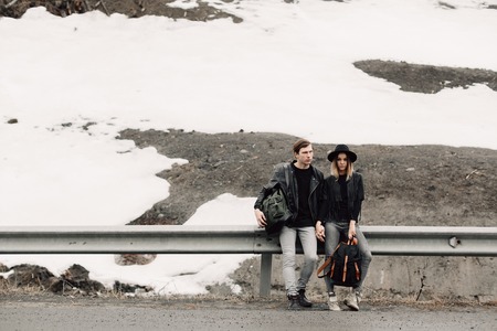 the couple are traveling. Boy and girl with backpacks travel. Loving couple near the road. Serious...