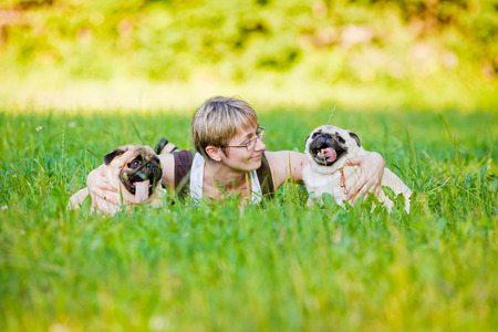 Nice blonde and cheerful young woman with her dogs resting on green lawn in the park の写真素材