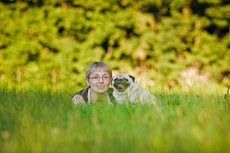 Nice blonde and cheerful young woman with her dog resting on green lawn in the park.の写真素材