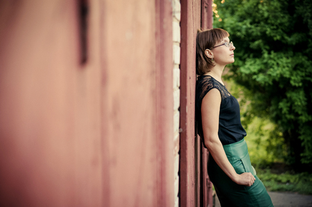 Portrait of a young beautiful woman with glasses and earrings standing against a wooden wall and looking up.の写真素材