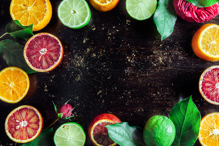 the red oranges, lime, yellow tangerines cut on pieces and whole lie on a wooden dark background with flowers of a rose, close-upの写真素材
